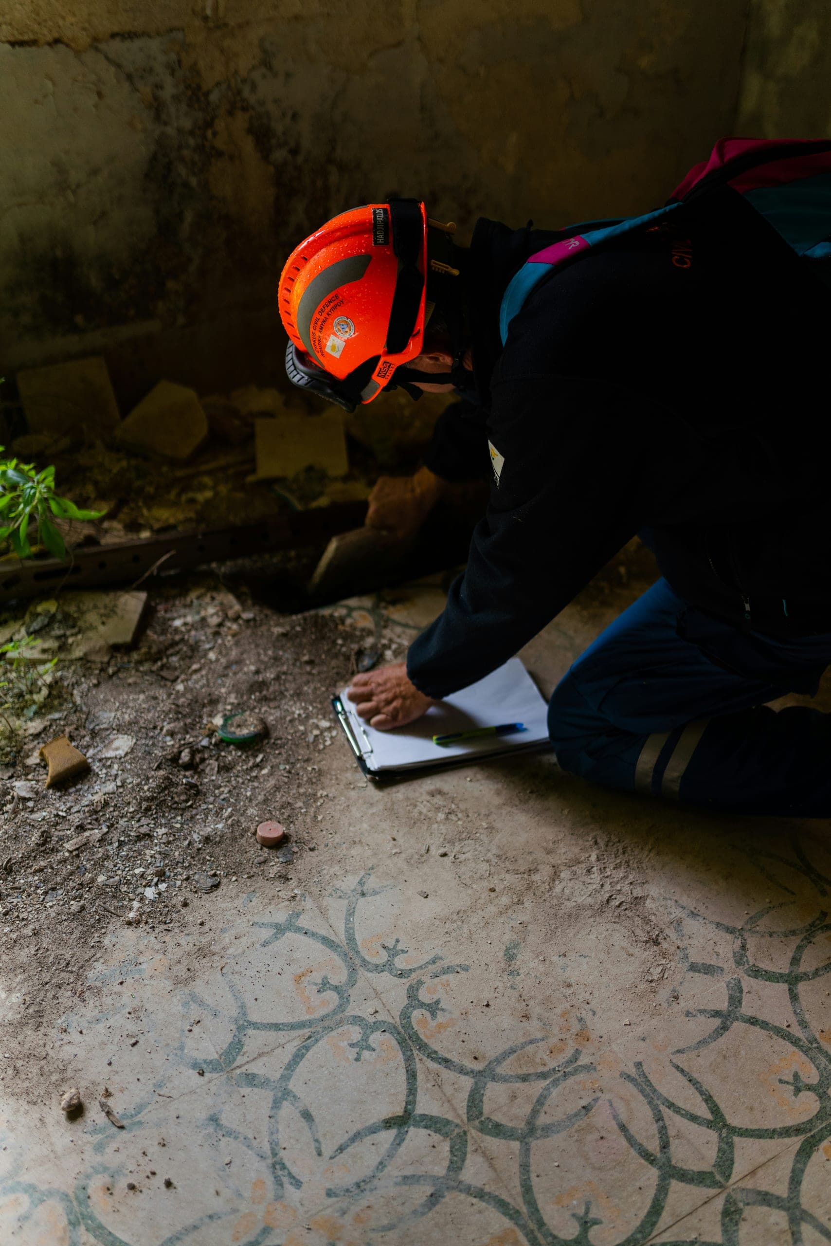 A surveyor kneeling on a bare floor, writing up findings on a clipboard